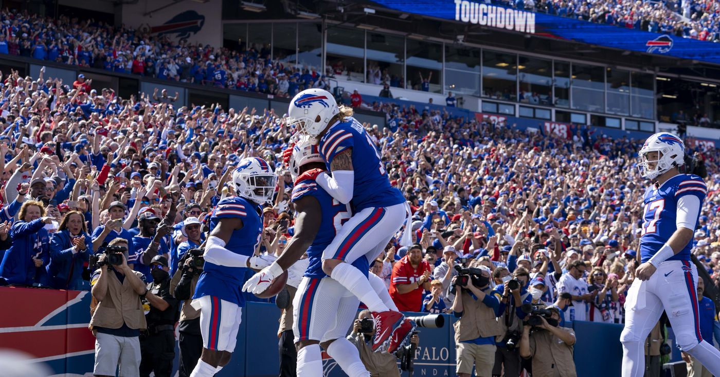 NFL players leap into each other celebrating a touchdown in the end zone as a packed stadium roars and a TOUCHDOWN sign lights up